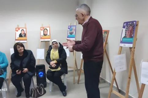 Participants sitting on chairs at an exhibit to give voices to people with cancer listening to a doctor