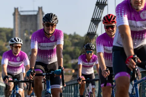 Group of cyclist in white and dark pink jerseys with the tower of a bridge in the background
