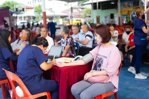 An Asian woman in pink shirt getting her blood pressure measured during a cancer outreach campaign in a public square
