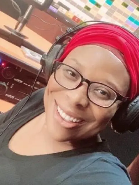 Black woman with red headscarf and wearing headphones smiles to the camera